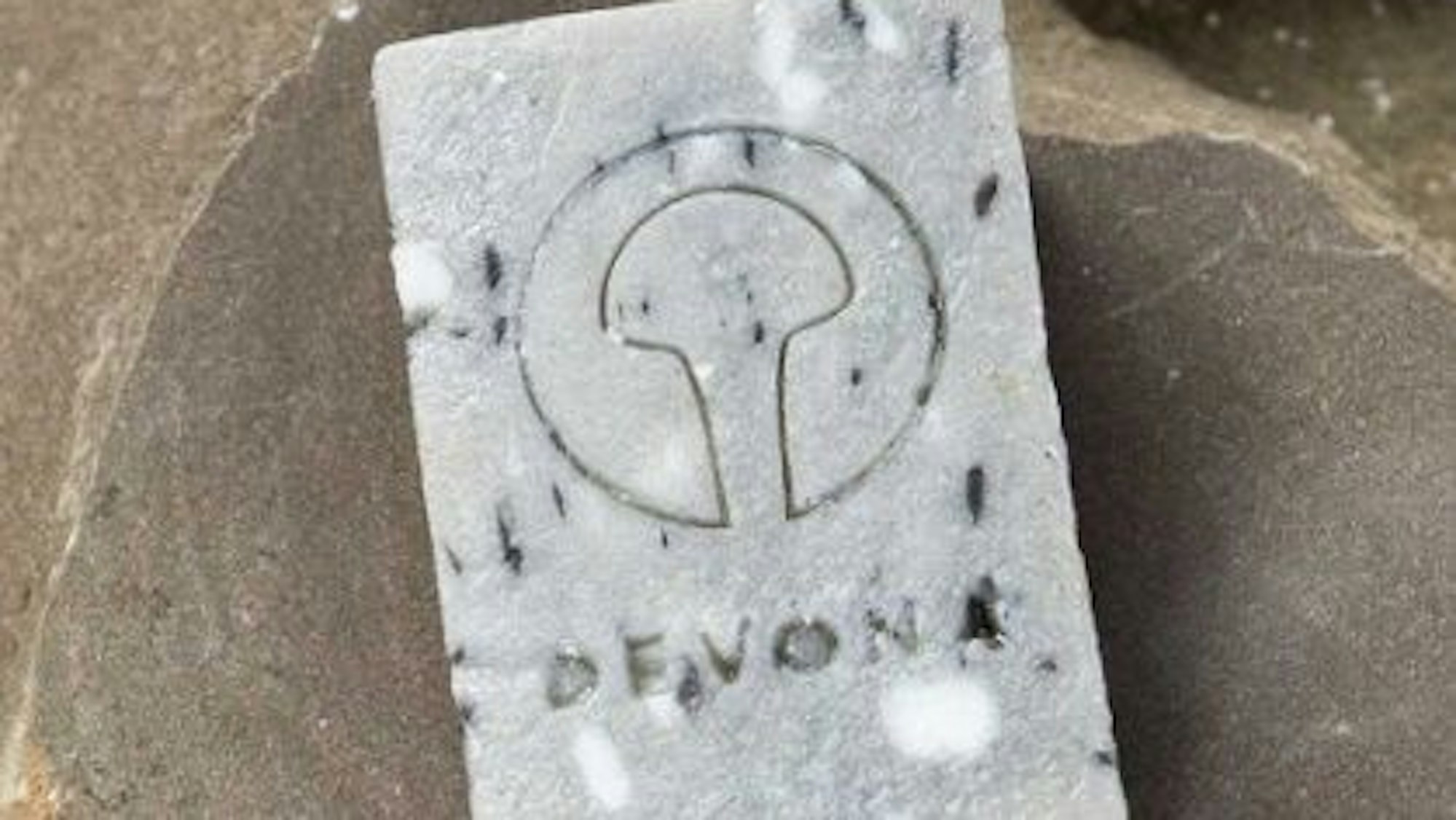 Eine Devona-Grauwackeseife liegt auf einem Grauwackestein.