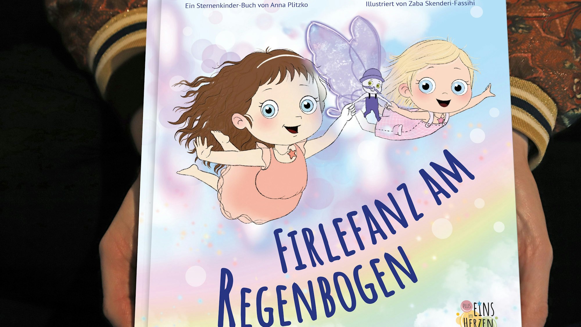 Zwei Hände halten ein Buch mit dem Titel Firlefanz am Regenbogen.