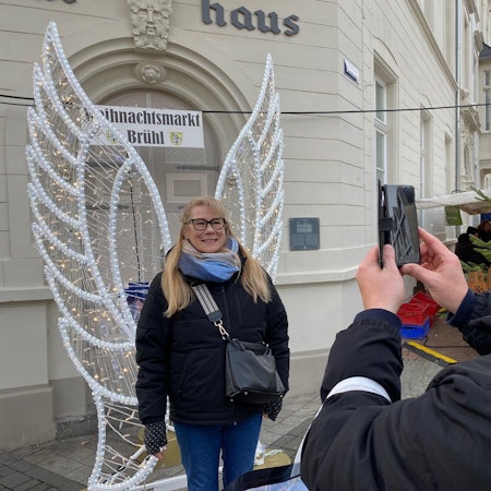 Zu sehen ist Heidi Feuersänger, die sich vor Engelsflügeln fotografieren lässt.