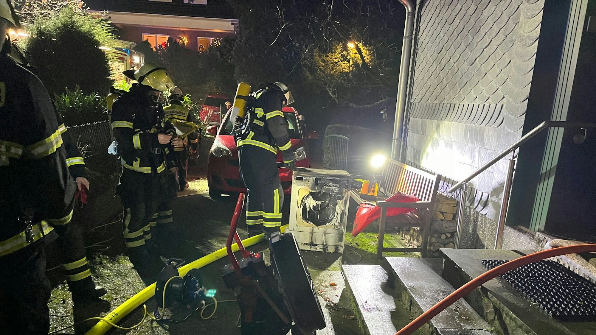 Einsatzkräfte löschen einen verschmorten Wäschetrockner vor einem Haus.
