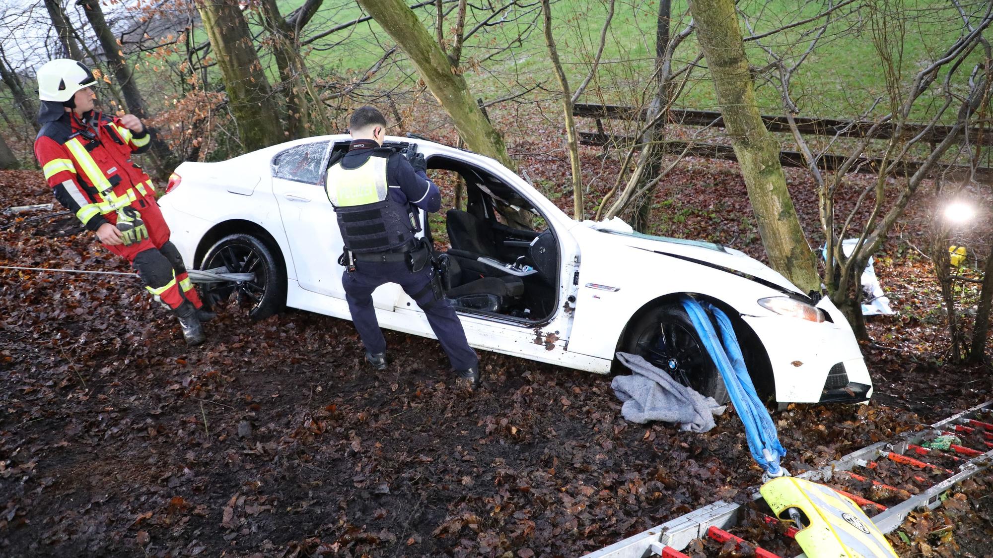 Die Feuerwehr hat ein in der Böschung an einem Baum stehende Fahrzeug gesichert. Ein Polizist macht Fotoaufnahmen.