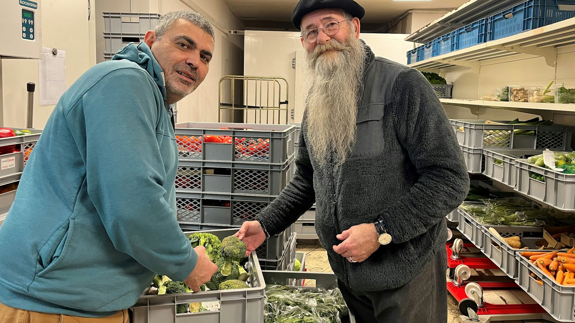 Die beiden Männer stehen zwischen Kisten und Regalen mit Gemüse.