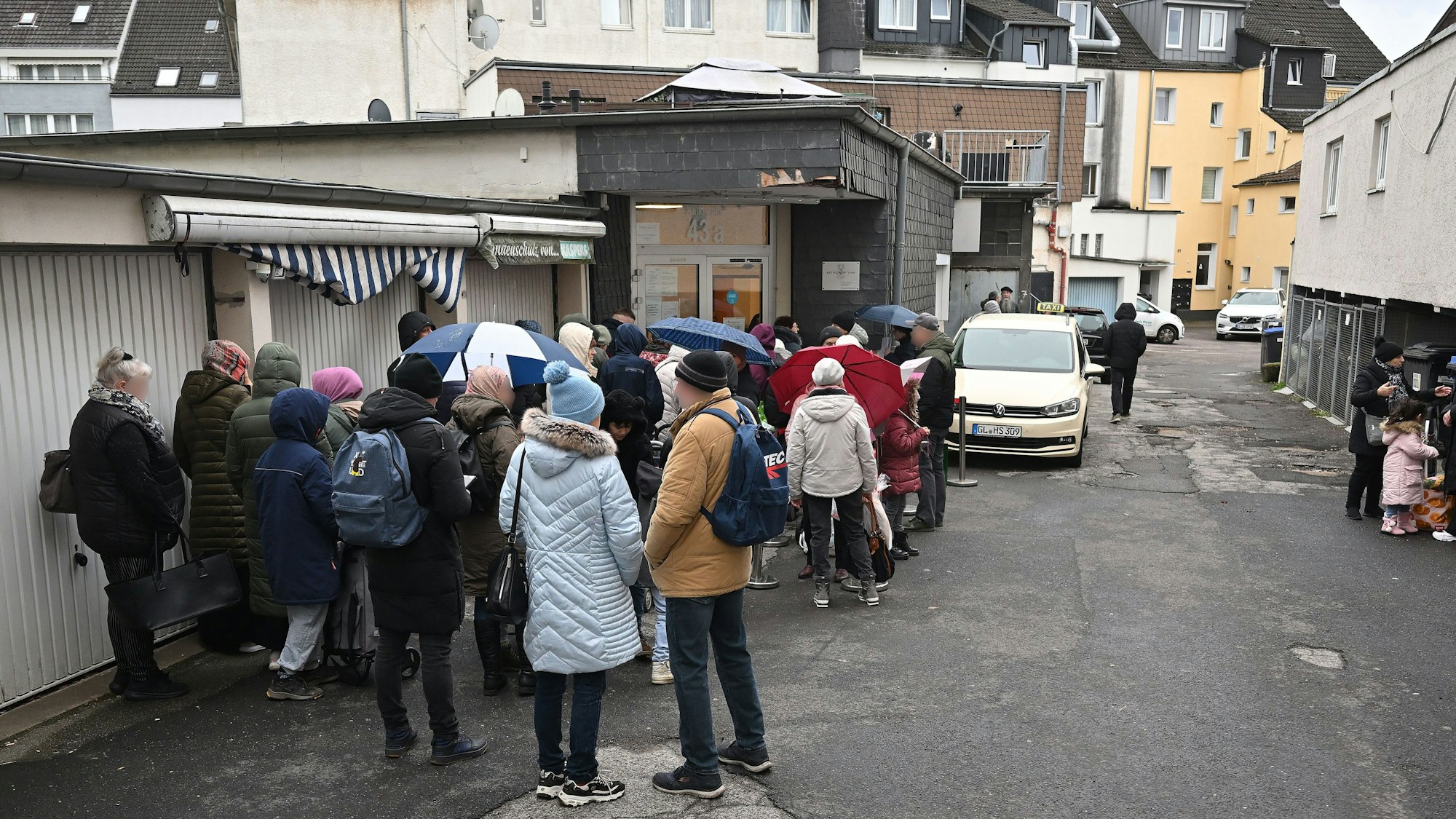 Die Menschen stehen hintereinander und warten vor der Eingangstür.