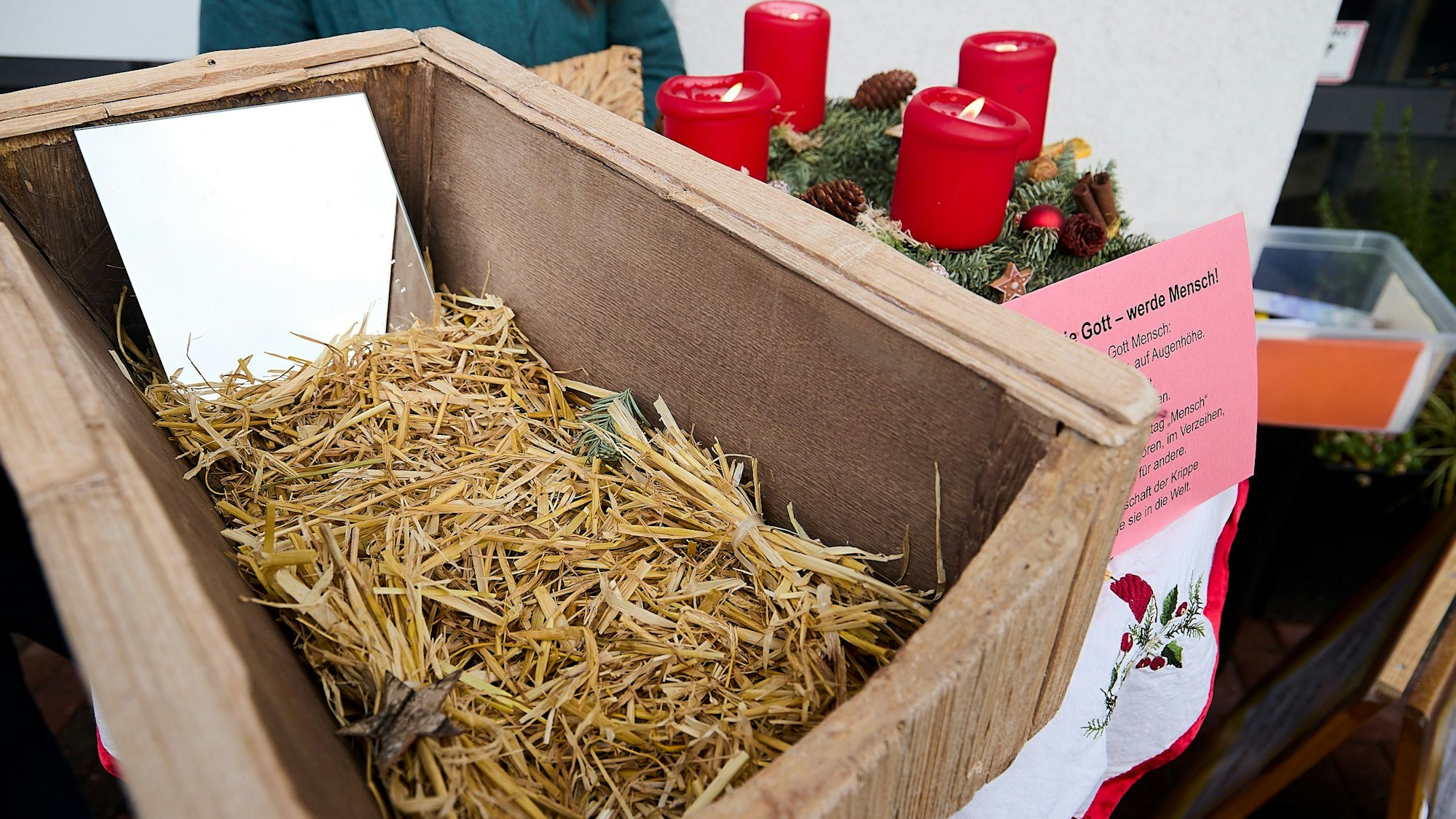 Neben einem Adventskranz steht eine Kiste auf einem Tisch. Darin sind etwas Stroh und ein Spiegel, um die Menschwerdung Gottes zu Weihnachten zu symbolisieren.