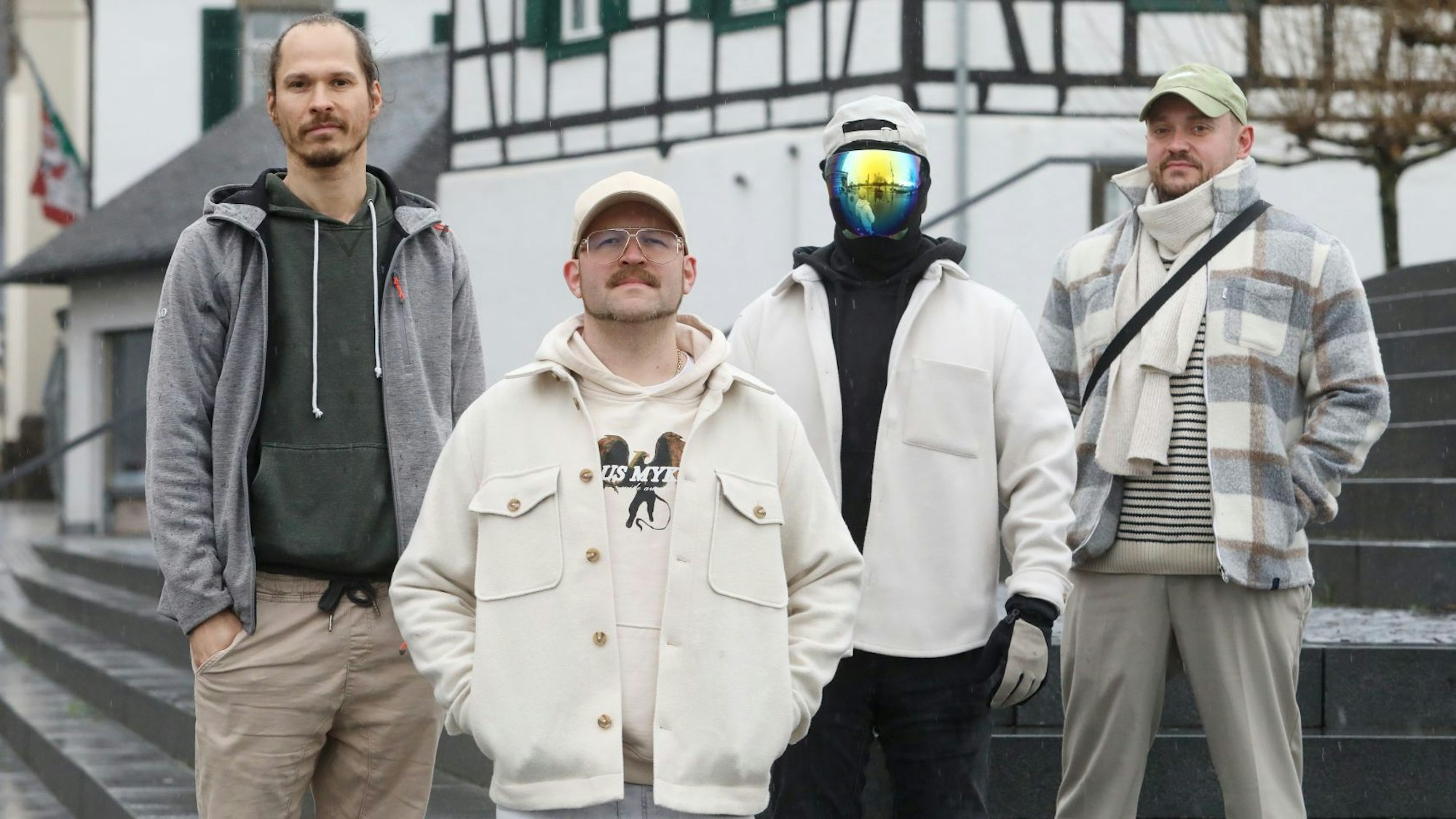 Vier junge Männer stehen auf einer Treppe, einer trägt eine Maske, die sein Gesicht verhüllt.