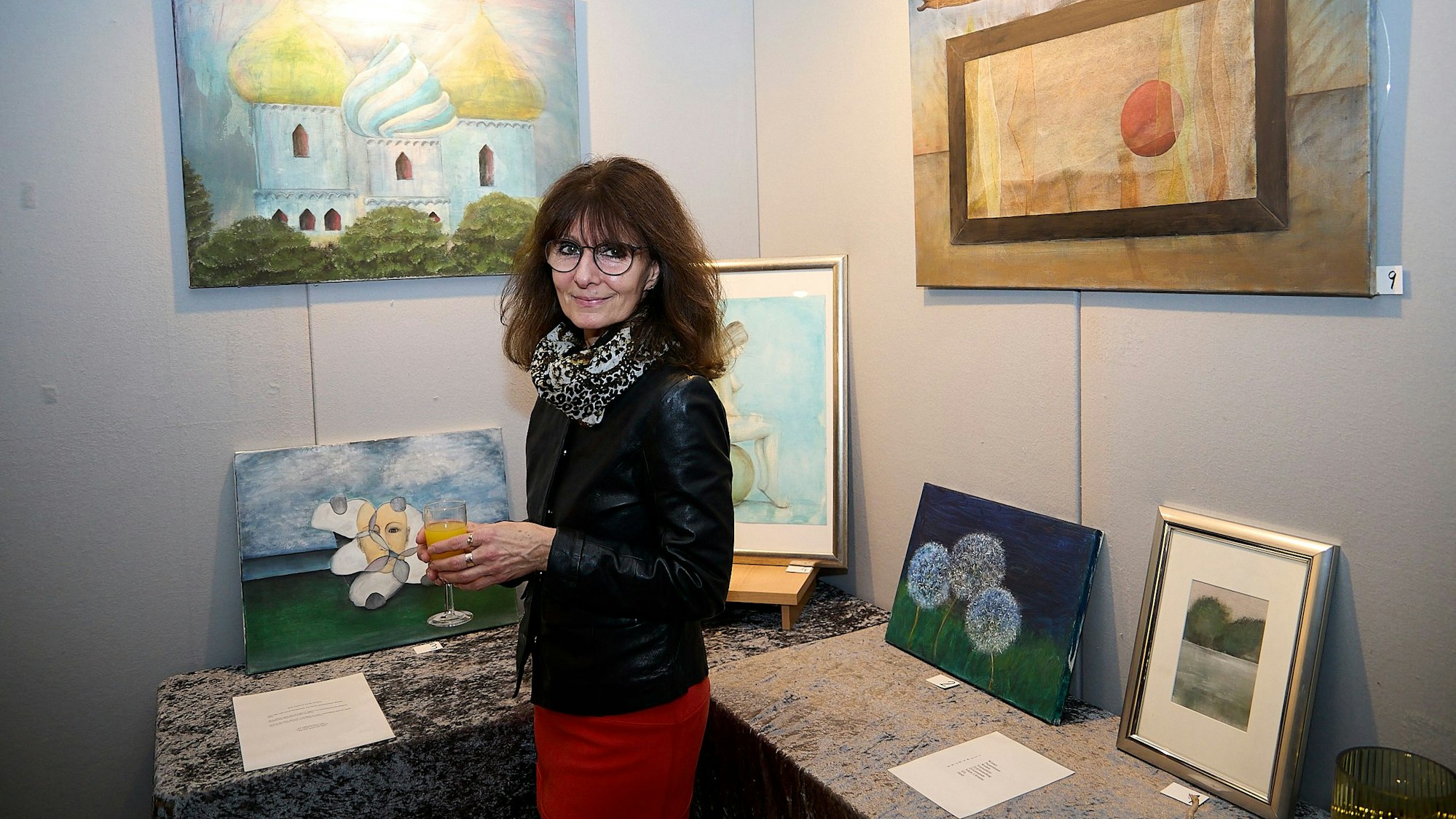 Das Bild zeigt die Künstlerin Uschi Wolkau vor einigen ihrer Bilder.