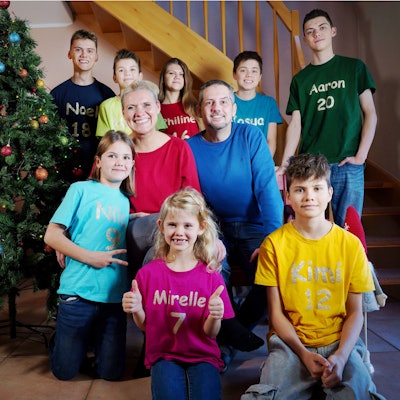 Katja und André Dederichs hocken neben einem Weihnachtsbaum. Vor und hinter ihnen sind ihre acht Kinder.