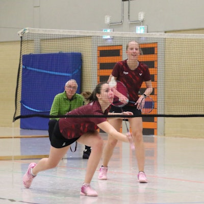 Nela-Sophie Wozny streckt sich, um einen Ball zu erreichen. Ihre Mitspielerin grinst. Dahinter sitzt ein Mann und schaut zu.