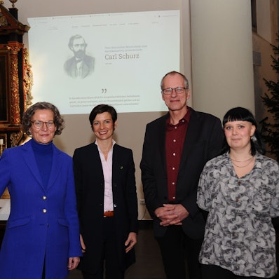 Drei Frauen und ein Mann stehen vor einer Leinwand in einer Kirche.