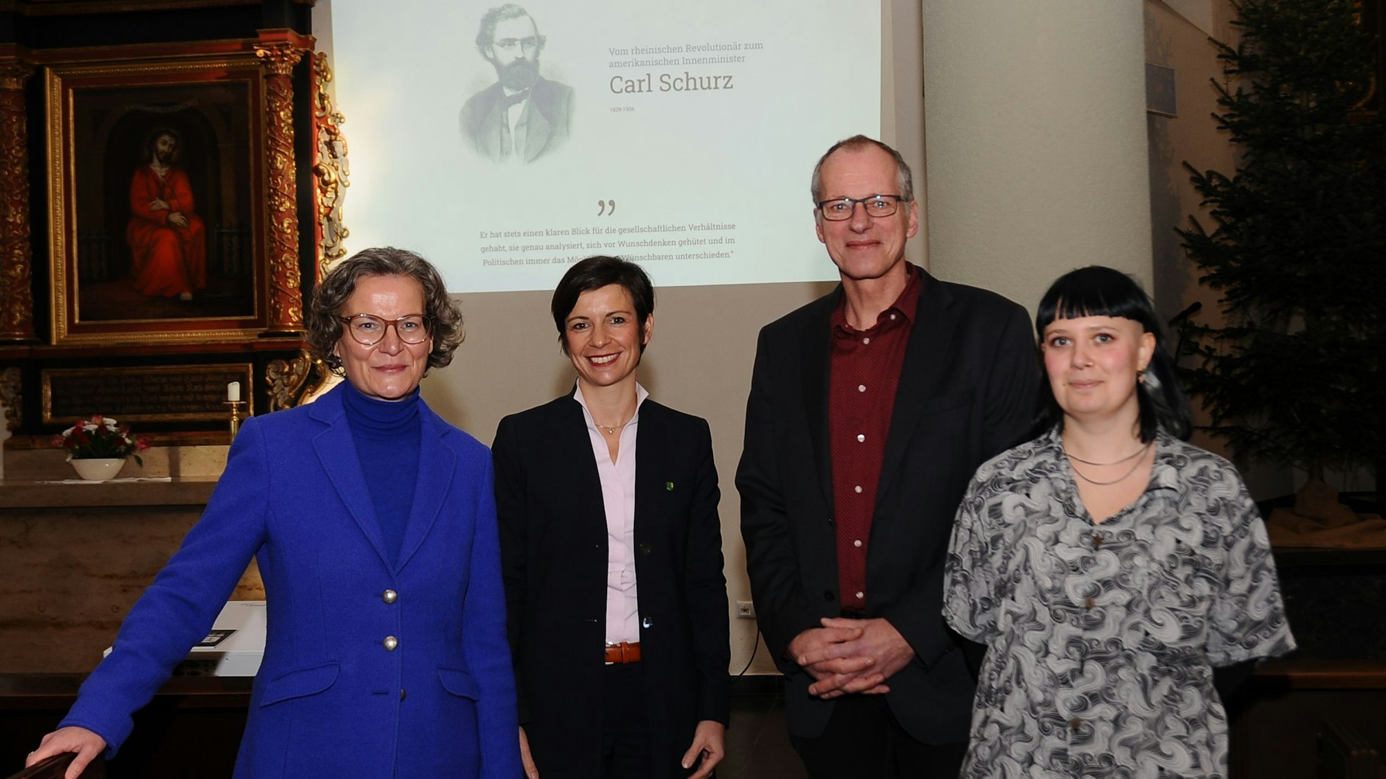 Drei Frauen und ein Mann stehen vor einer Leinwand in einer Kirche.