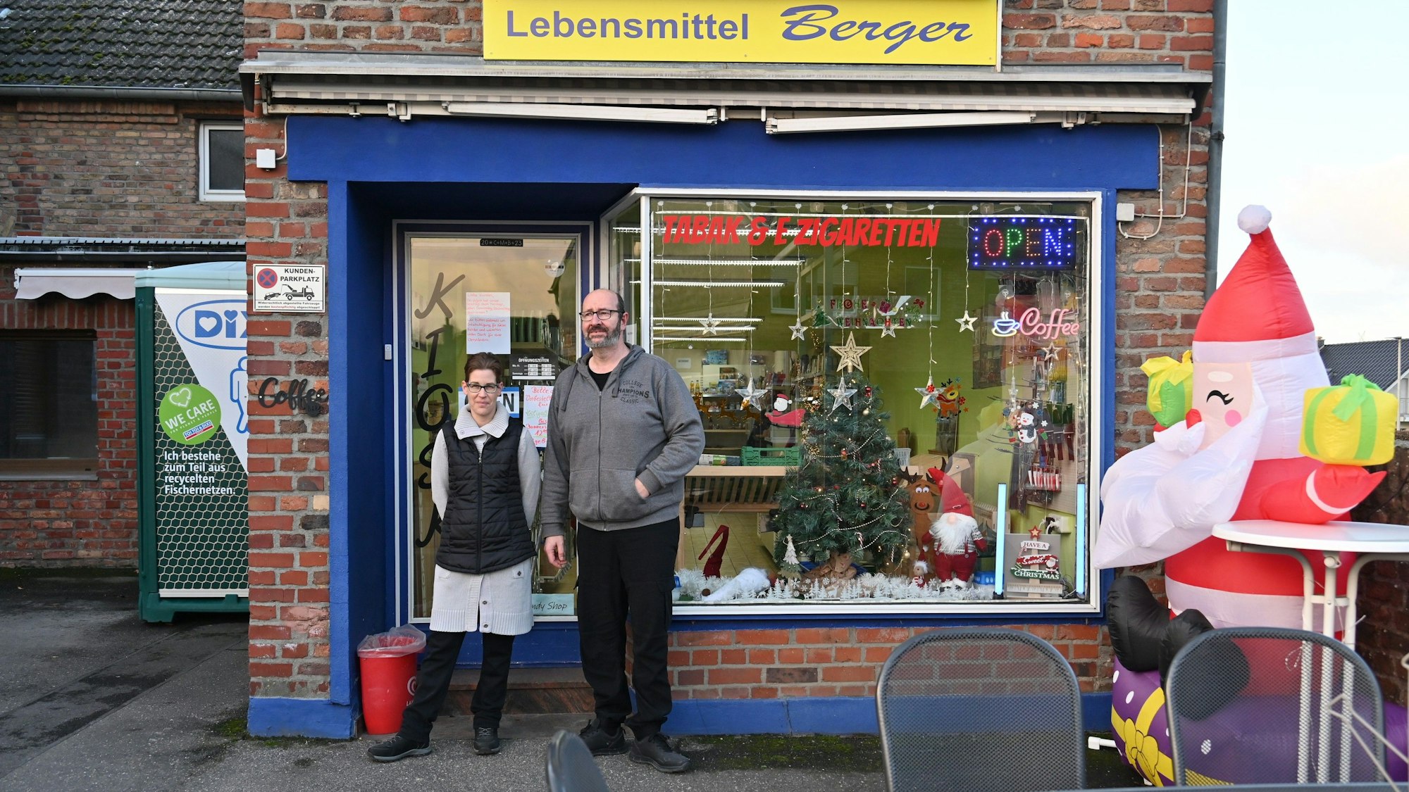 Die Angestellte Yvonne Juris und Jochen Berger stehen vor dem Kiosk, der für die Weihnachtszeit dekoriert ist. Über dem Schaufenster hängt ein Schild mit der Aufschrift Lebensmittel Berger.