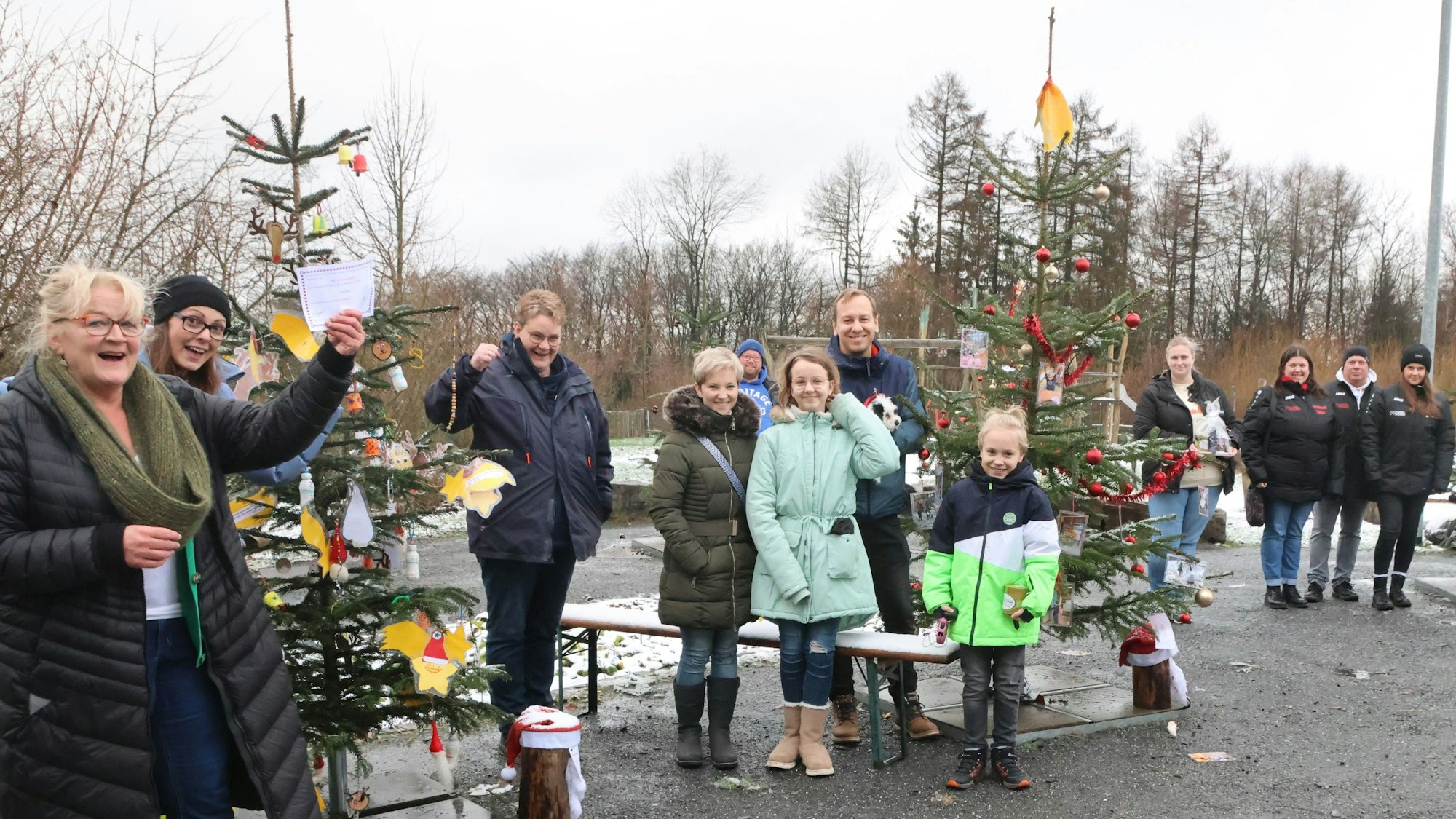 Das Foto zeigt originell geschmückte Weihnachtsbäume und lachende Menschen.