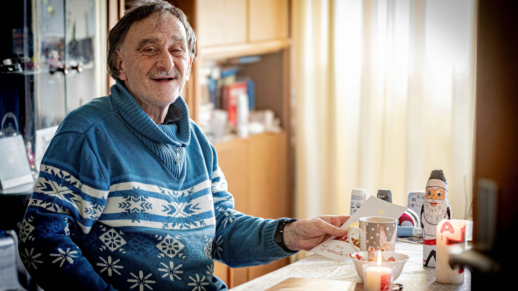 Wieder ein menschenwürdiges Leben hat Peter M. nach langen Jahren auf der Straße. Er sitz an seinem Tisch in einem blau-weißen Winterpulli, eine Kerze vor ihm und eine Tasse Tee.