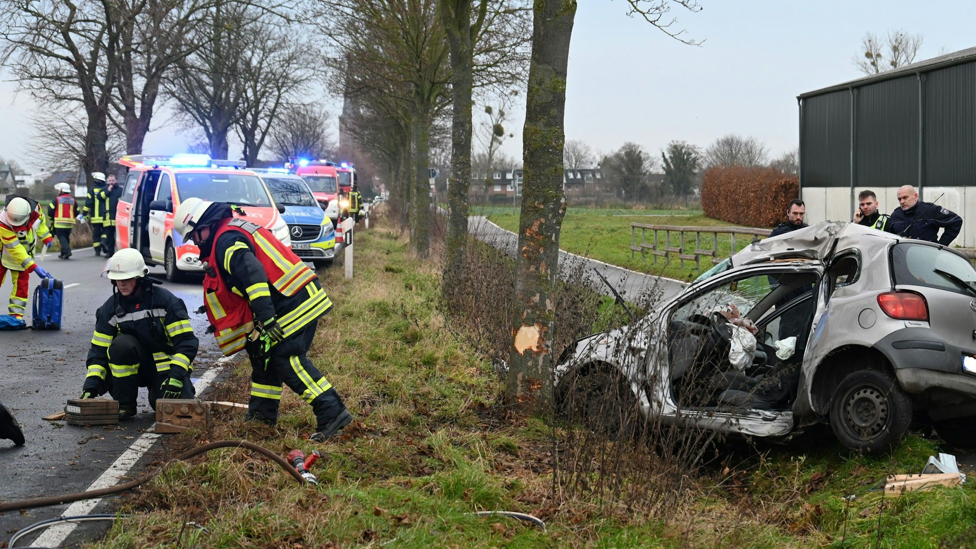 Das Bild zeigt die Unfallstelle mit mehreren Feuerwehrleuten und Rettungssanitätern.
