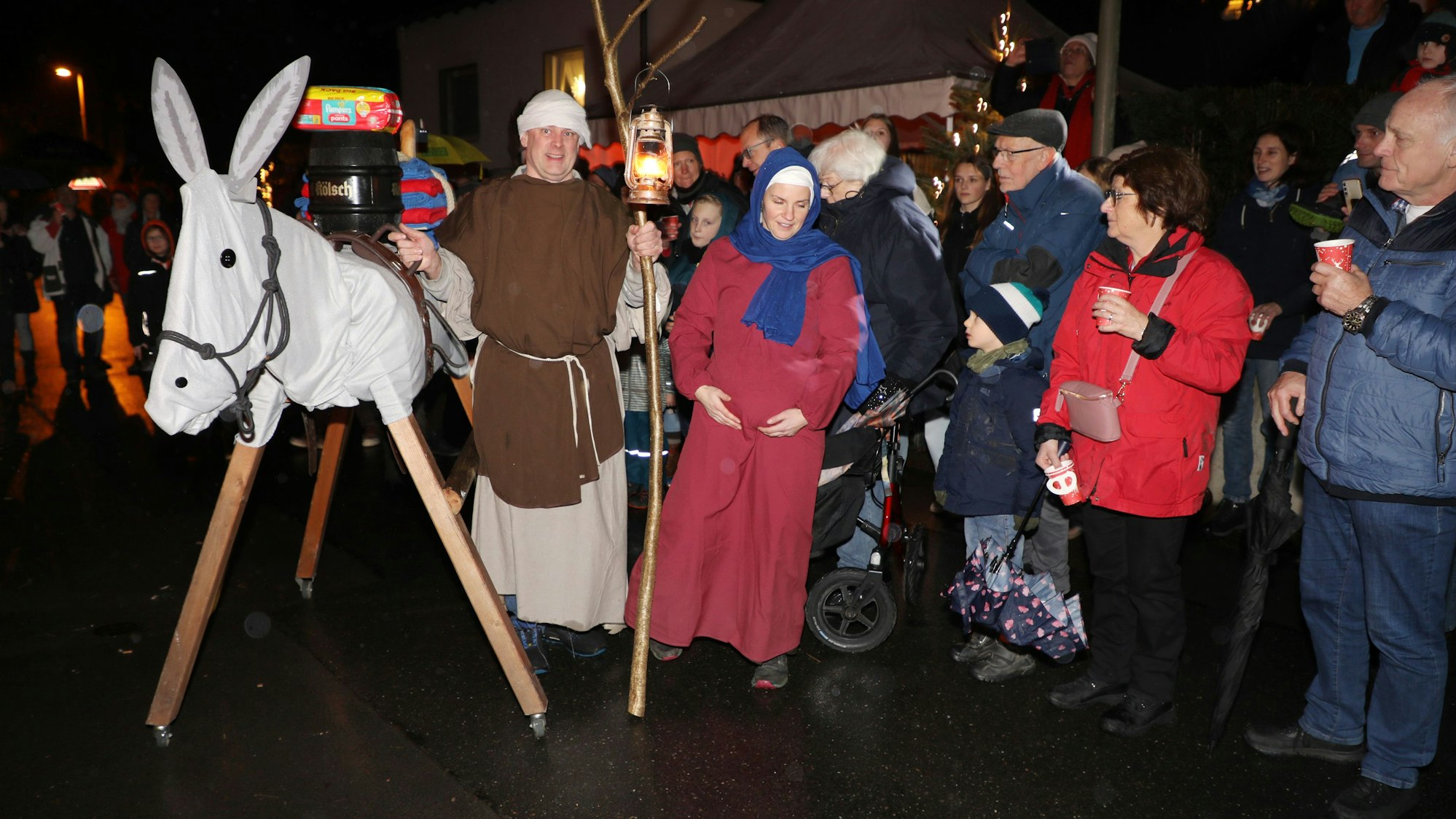 Maria und Josef ziehen mit einem Holzesel über eine Straße, die von Menschen gesäumt ist.
