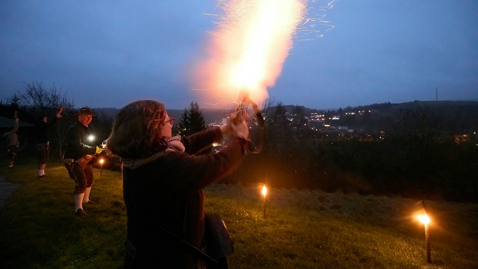 Die Böllerschützen haben sich am Hang positioniert und feuern ihre Büchsen ab. Pechfackeln beleuchten die Szenerie.