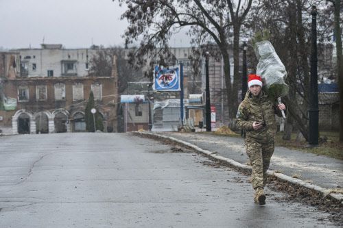 Ein ukrainischer Soldat mit Weihnachtsmütze trägt einen Tannenbaum durch eine Straße der Region Charkiw.