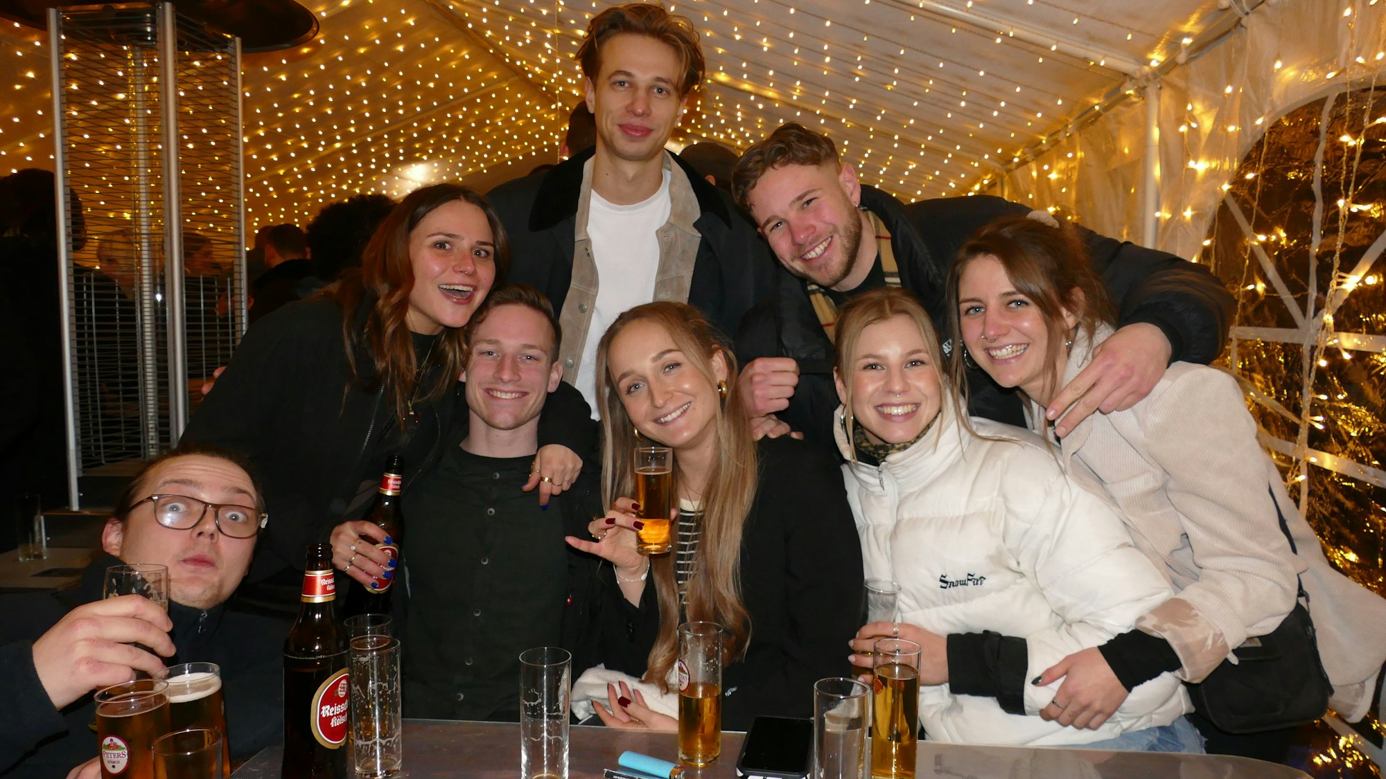 Junge Leute in einem Partyzelt, sie sind guter Stimmung und lachen in die Kamera.