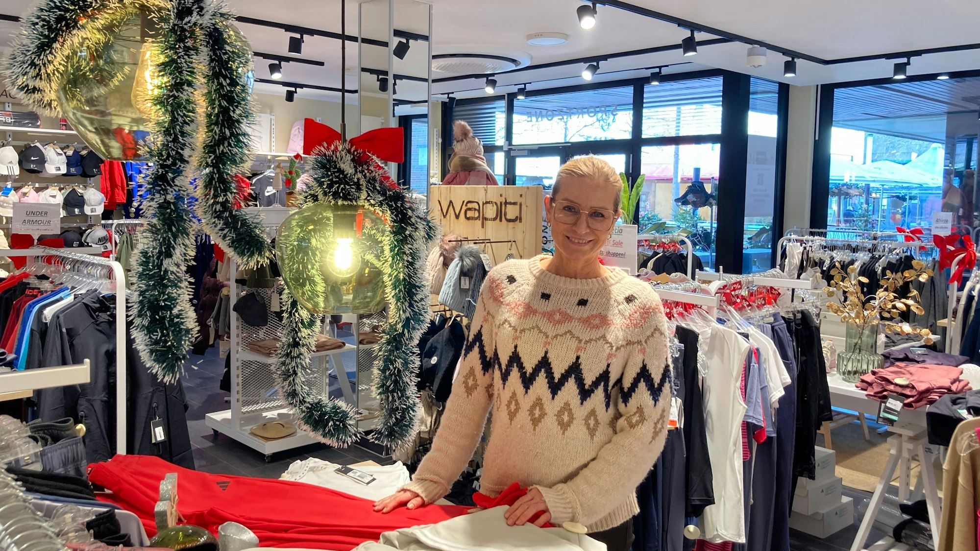Eine Frau in einem Pulli steht in einem Geschäft mit Anziehsachen.