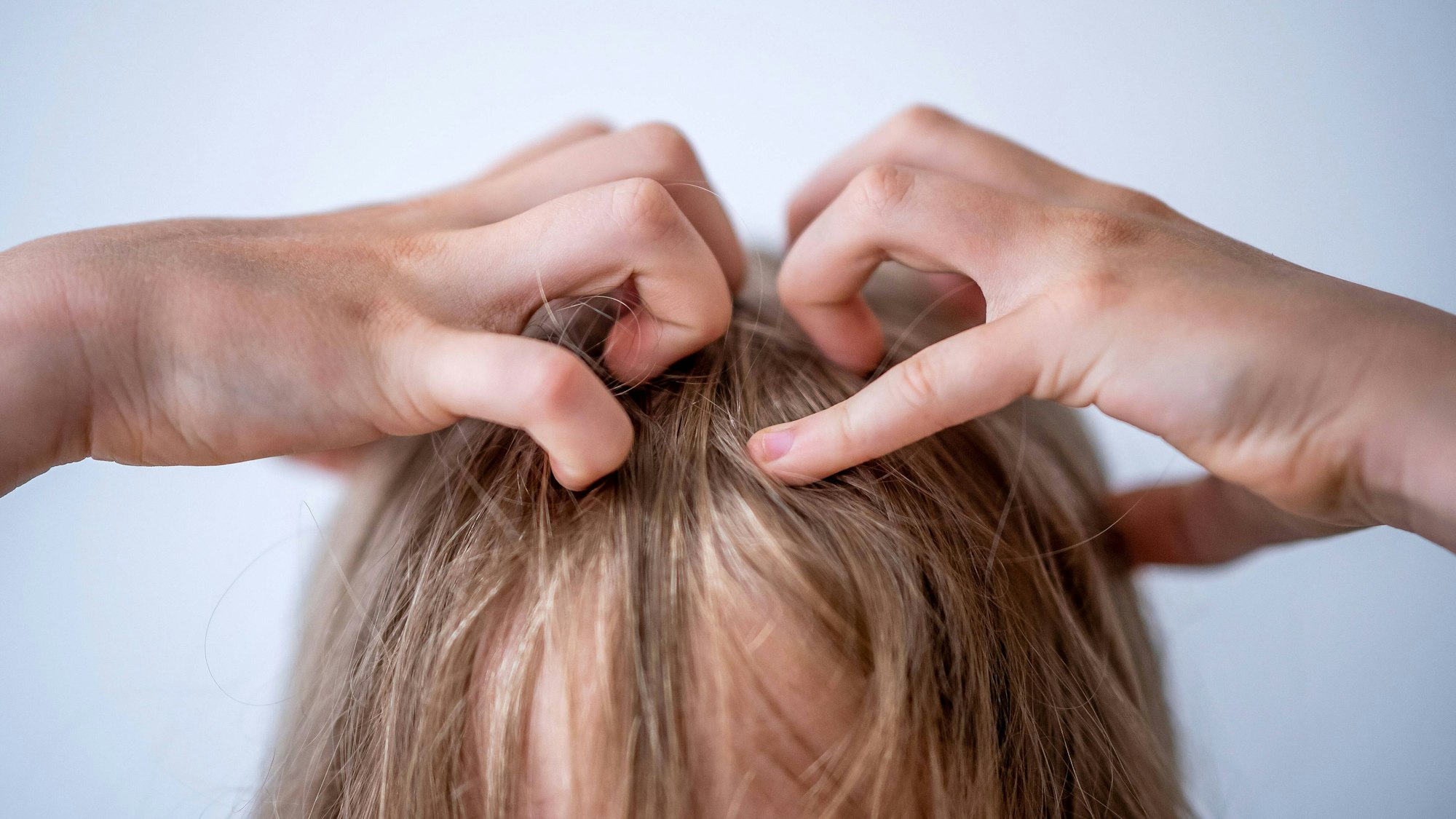 Ein Kind mit langen Haaren kratzt sich am Kopf.