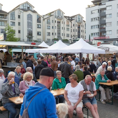Menschen sitzen auf Bierbänken vor Pavillons.