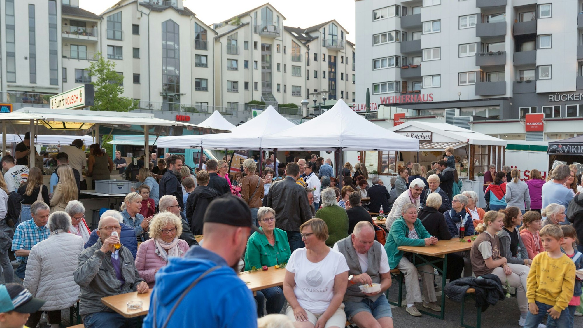 Menschen sitzen an Biertischen und stehen an zahlreichen Imbissbuden.