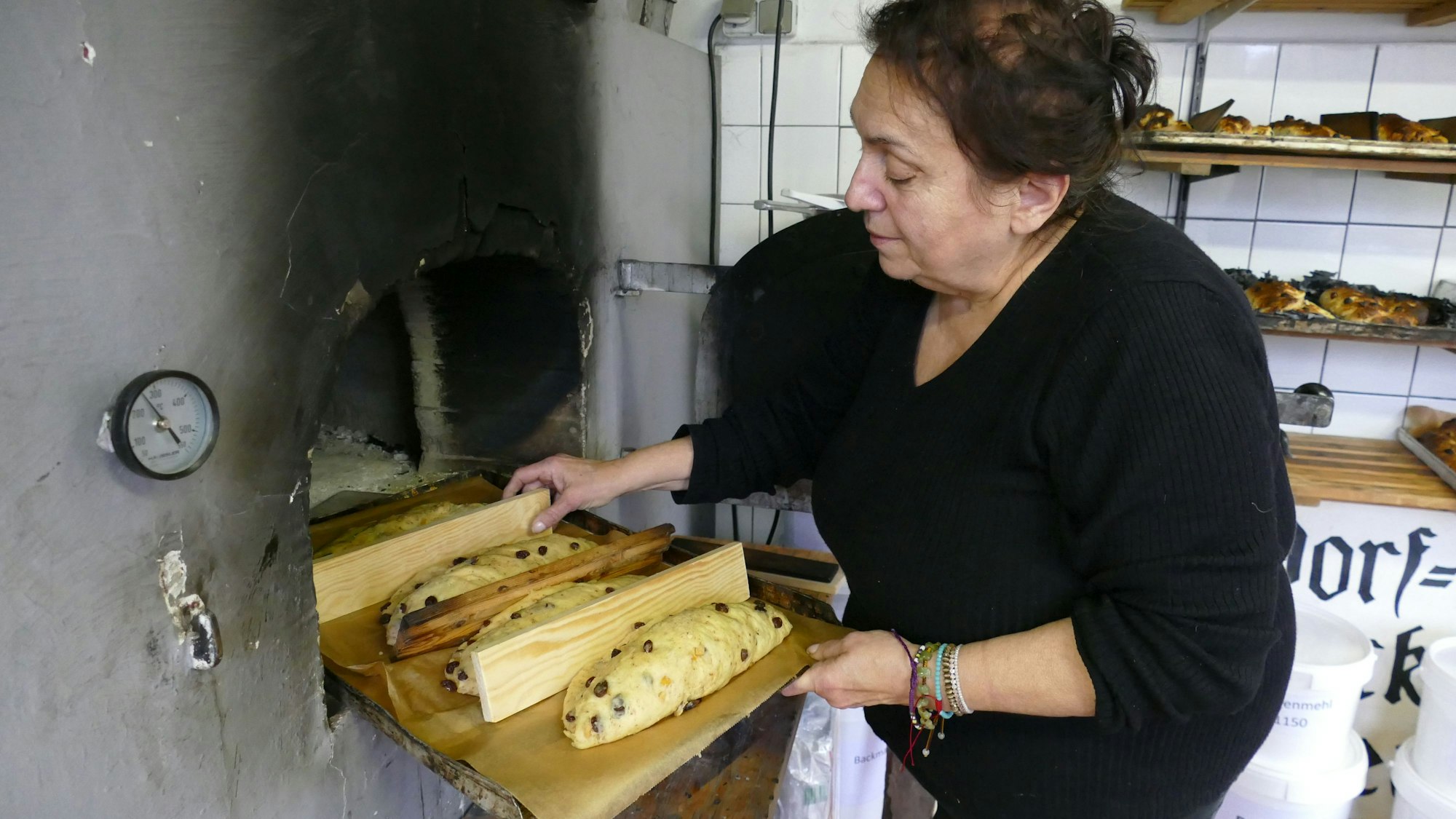 Eine Frau schiebt Stollen in einen alten Backofen.