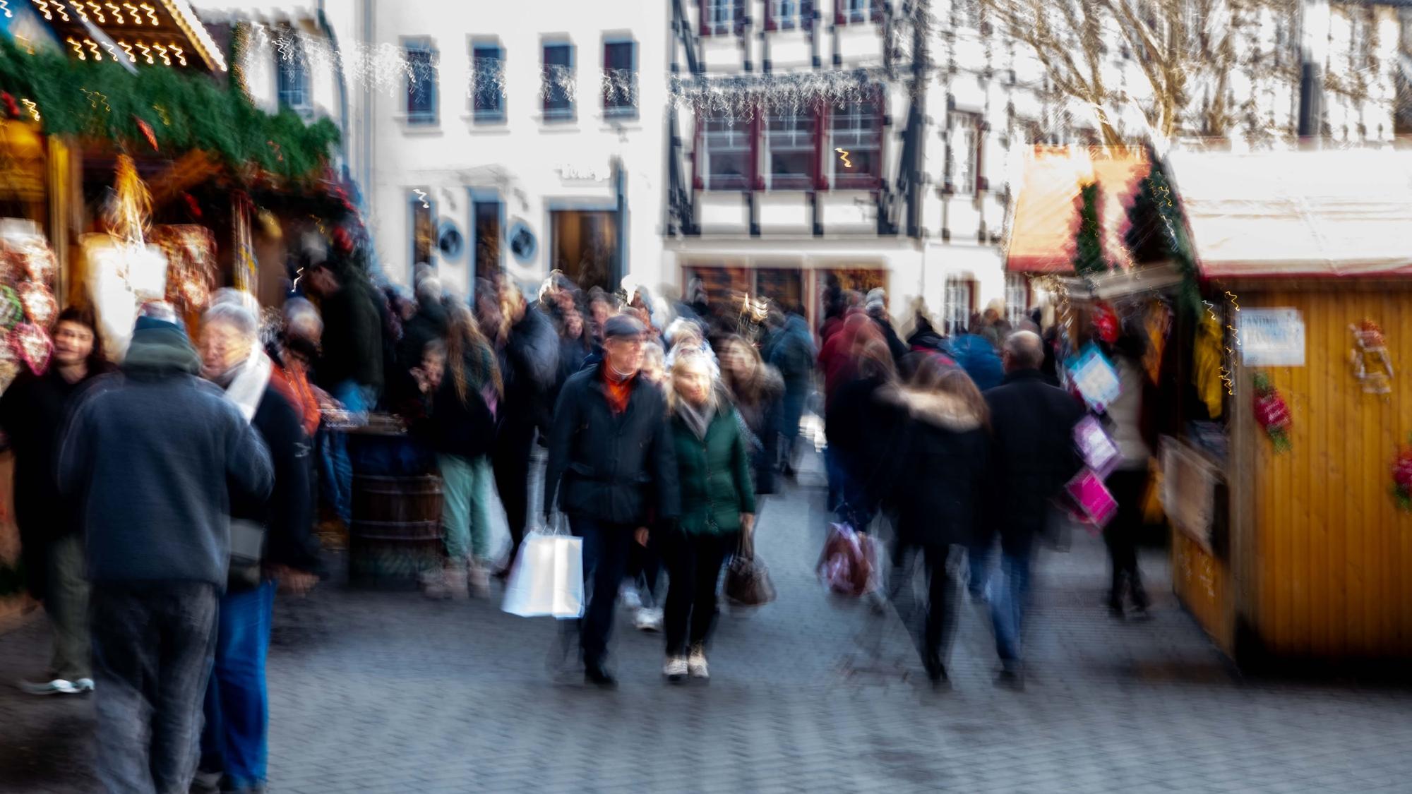 Leute shoppen und schlendern über den Weihnachtsmarkt. Die Aufnahme ist verschwommen, um die Menschen unkenntlich zu machen.