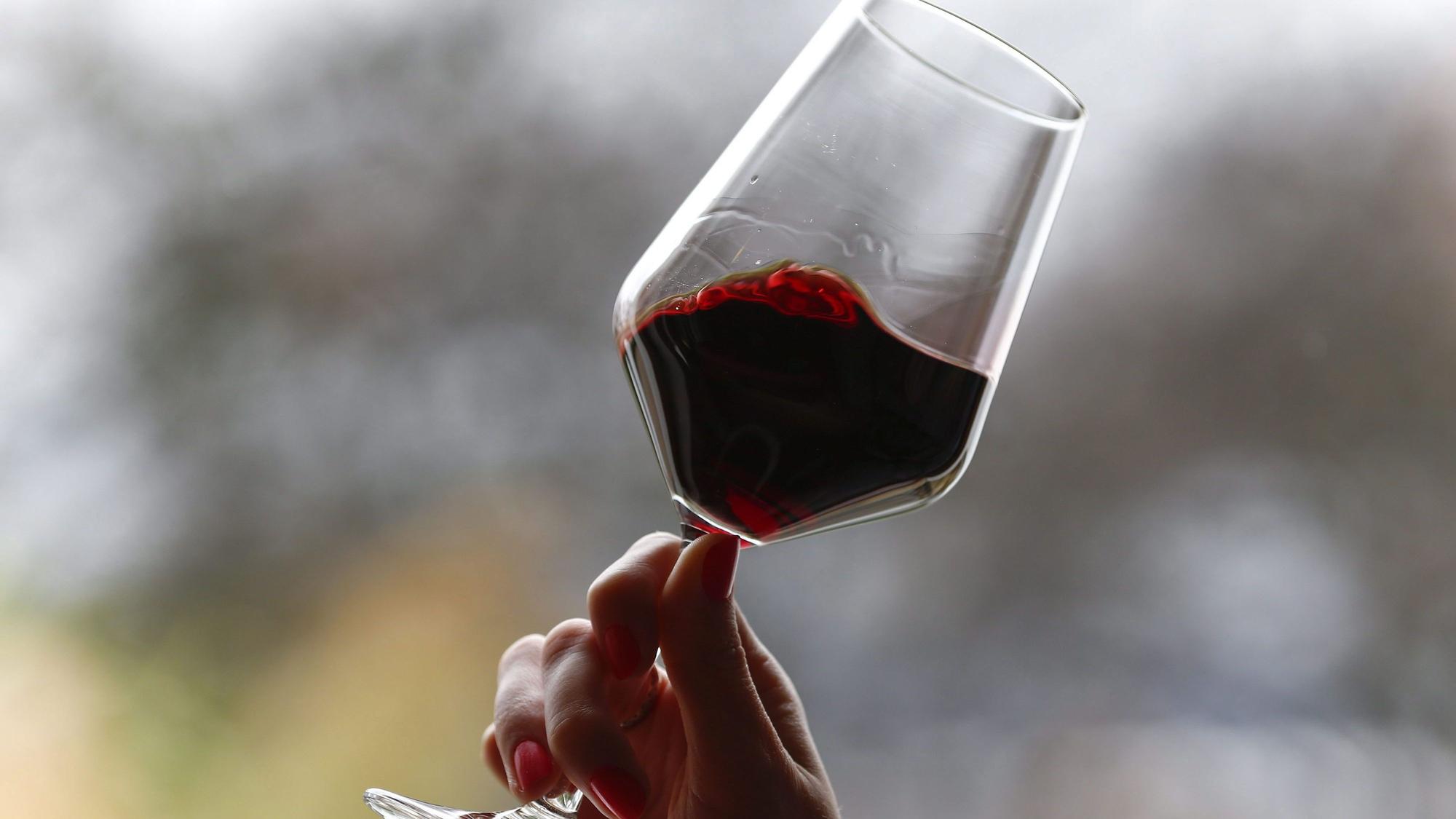Eine Hand hebt ein Glas Rotwein und lässt die Flüssigkeit im Glas schwingen.