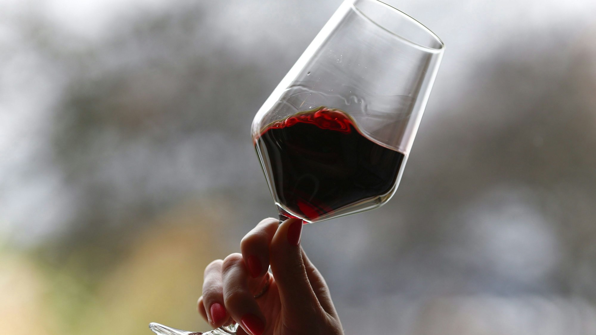 Eine Hand hebt ein Glas Rotwein und lässt die Flüssigkeit im Glas schwingen.