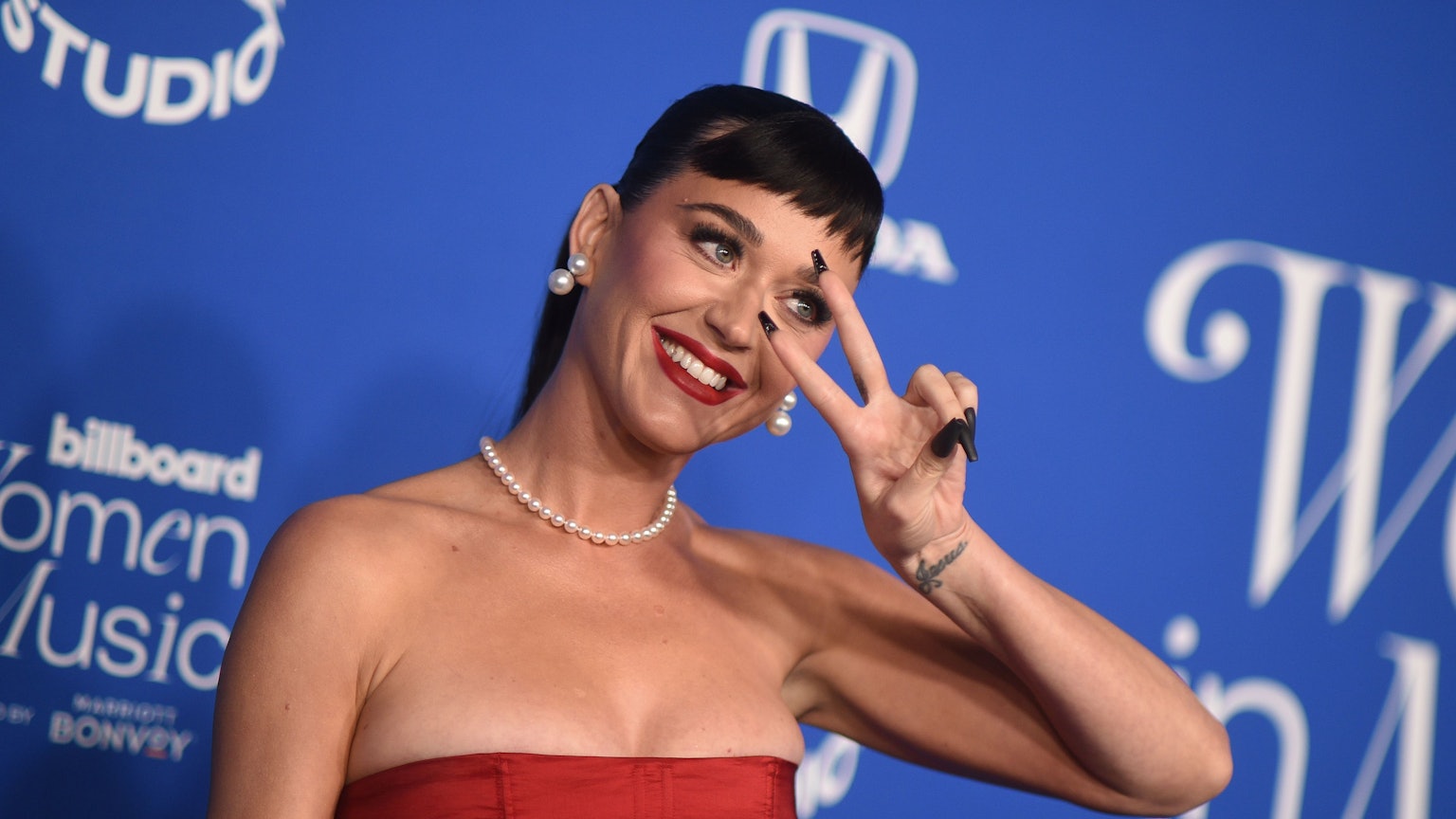 Katy Perry steht in einem roten Kleid vor einem blauben Hintergrund