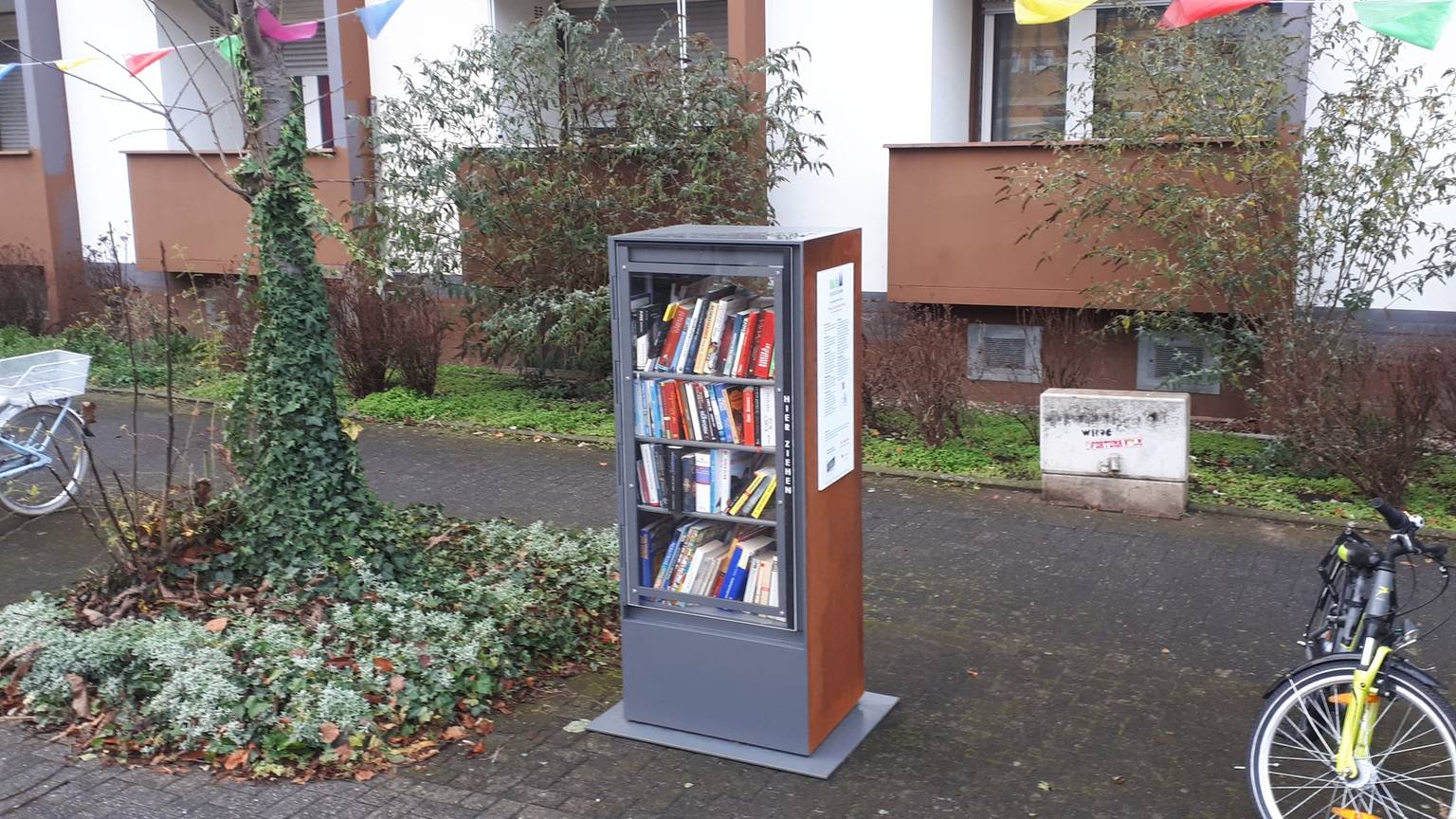 Ein Bücherschrank steht neben einem Baumbeet.