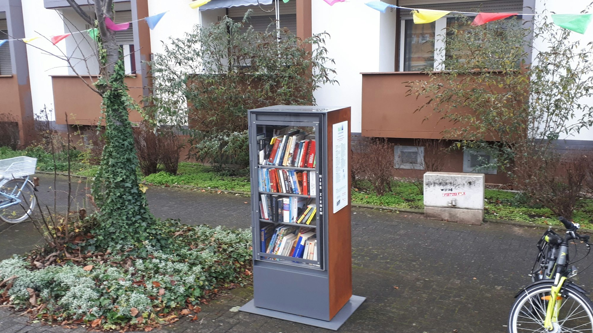 Ein Bücherschrank steht neben einem Baumbeet.