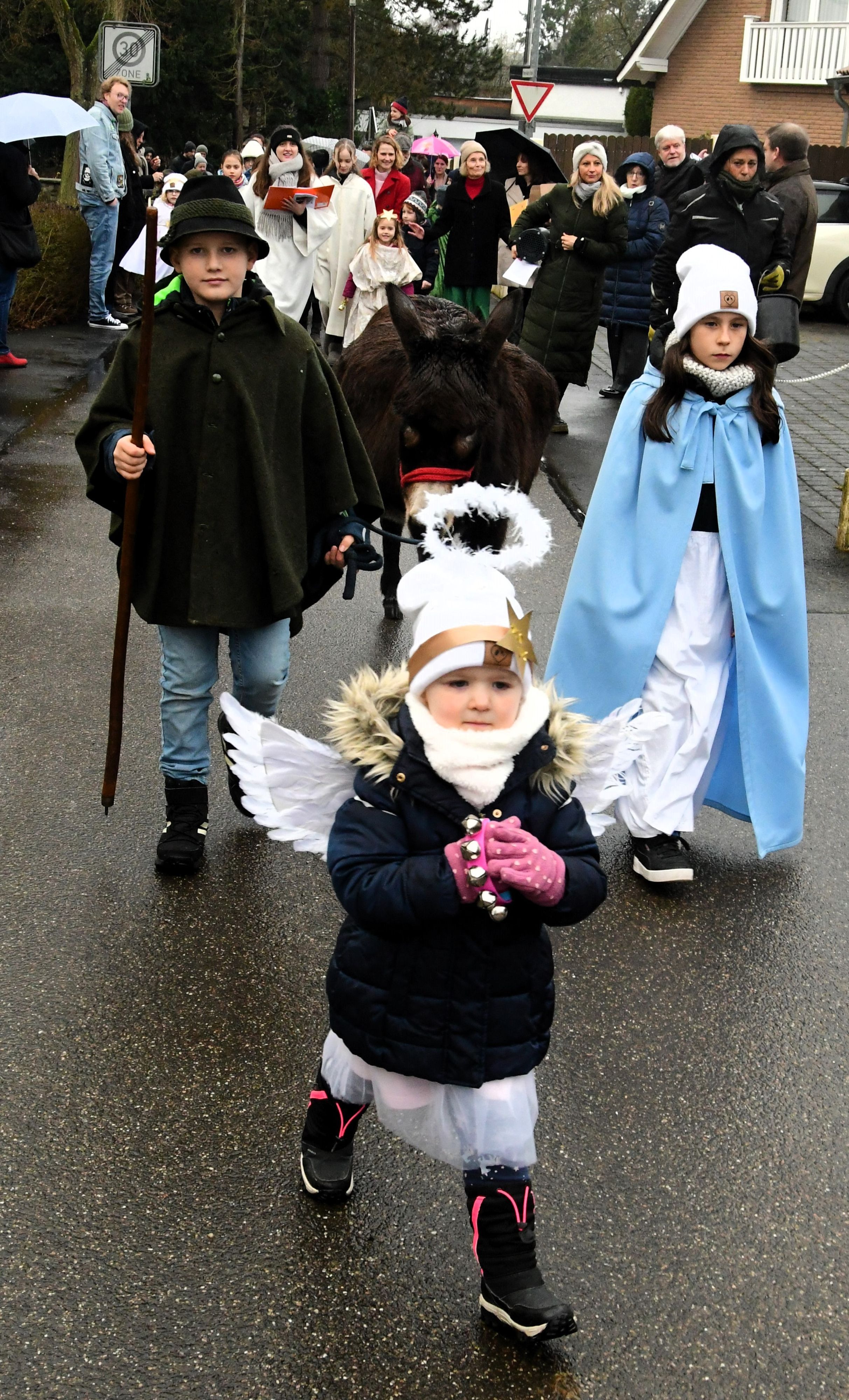 Drei Kinder stellen bei einem Krippenspiel einen Engel, Maria und Josef dar. Sie führen auch einen Esel.