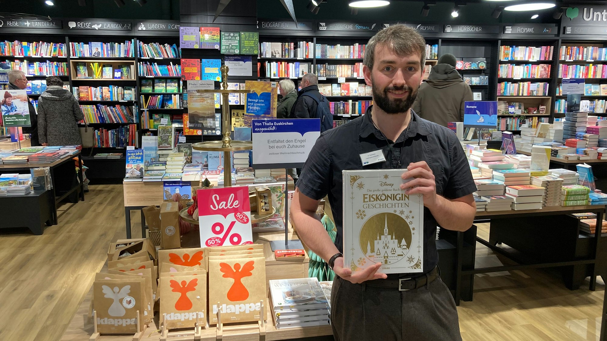 Ein Mann hält ein Buch vor sich. Er steht in einem Buchladen vor reduzierten Artikeln.