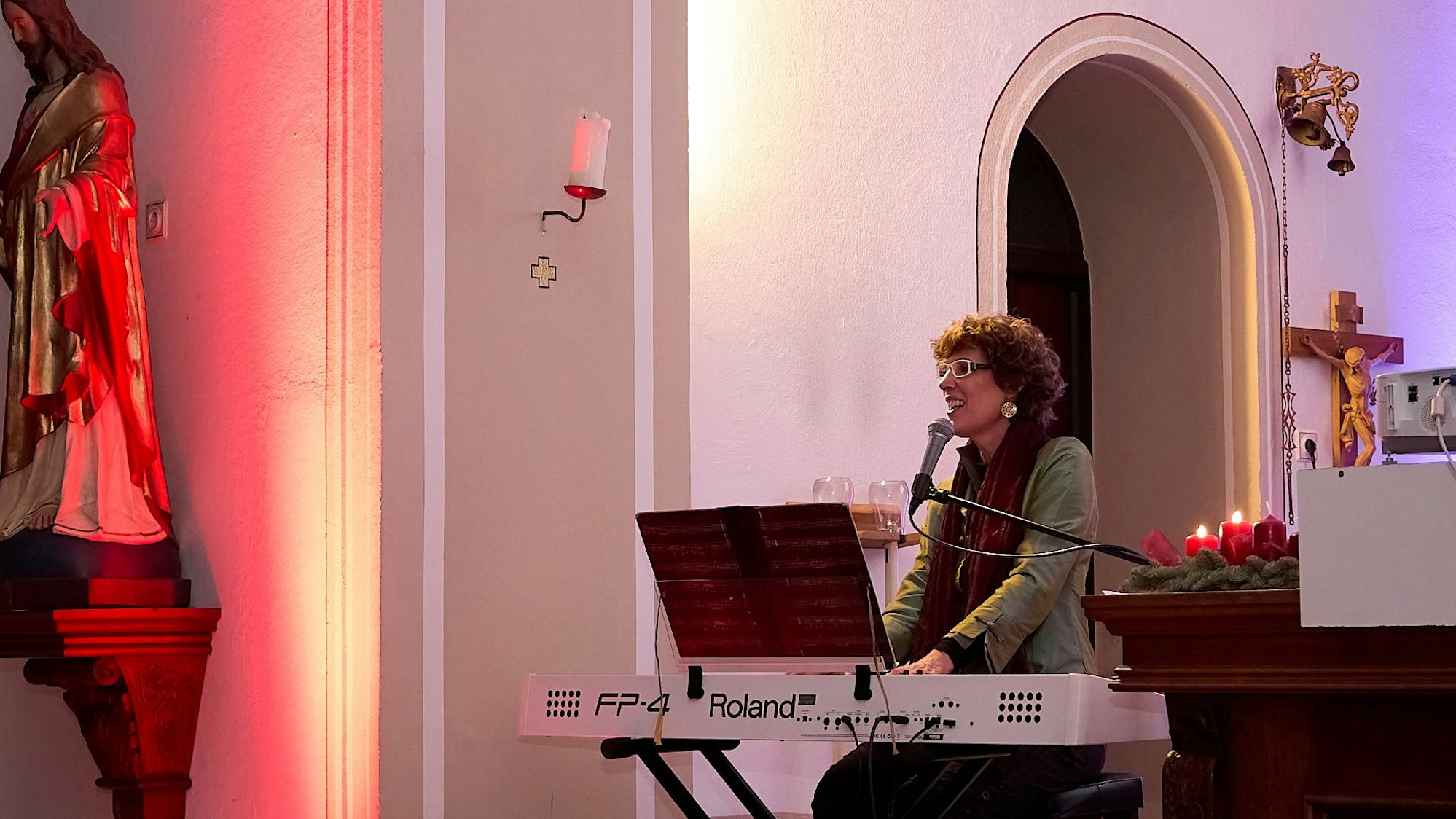 Die Kölner Sängerin Kathrin Eigendorf sitzt in einer Kirche an einem weißen E-Piano und singt in ein Mikrofon.