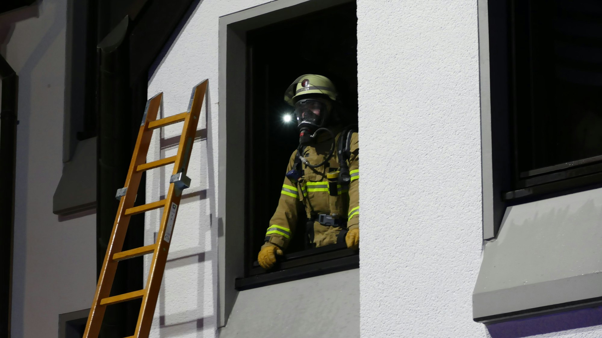 Ein Feuerwehrmann mit Atemschutz schaut aus einem Fenster der Brandwohnung.