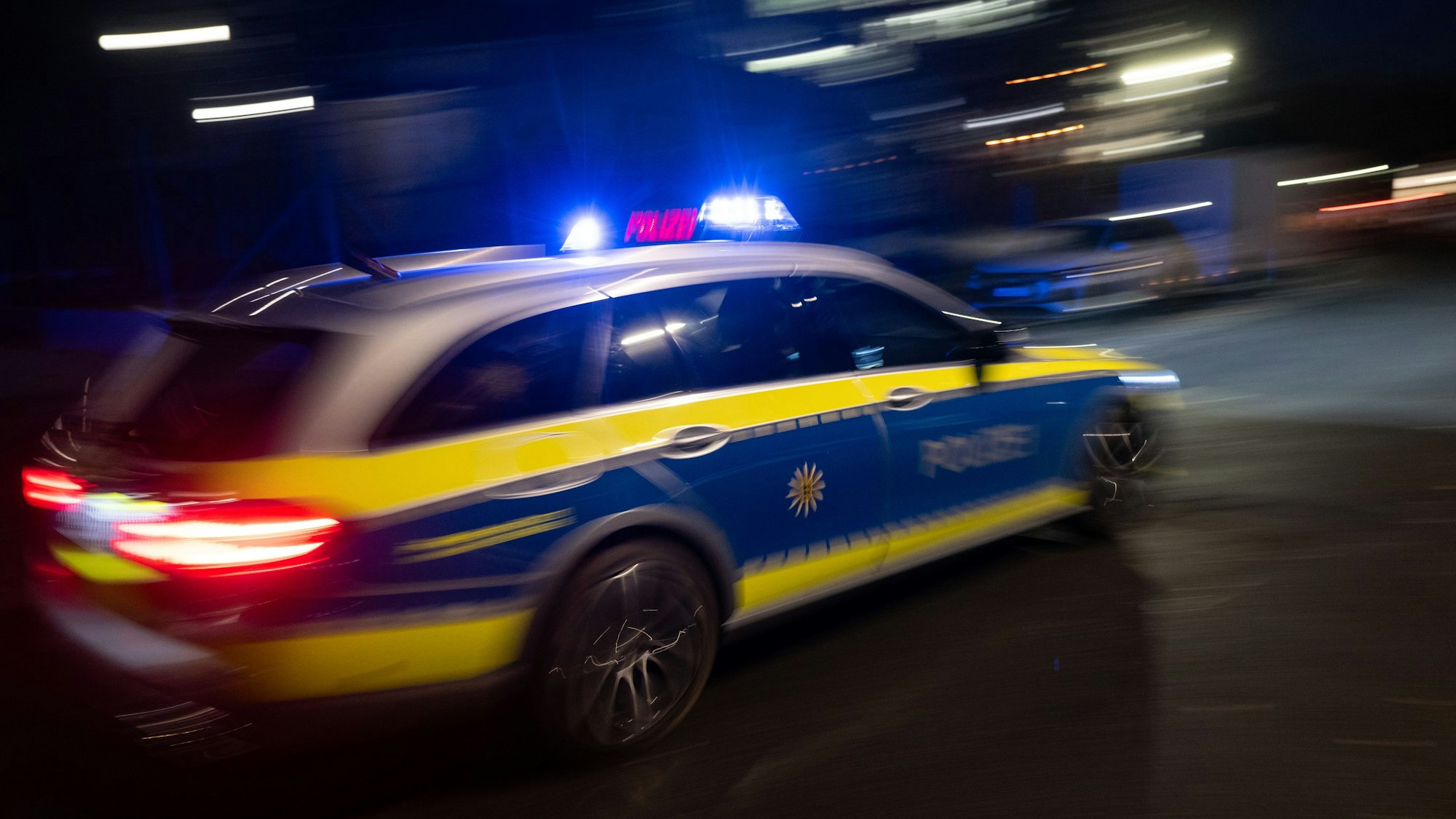 Ein Polizeifahrzeug fährt im Rahmen eines Fototermins mit Blaulicht an einem Gebäude vorbei.