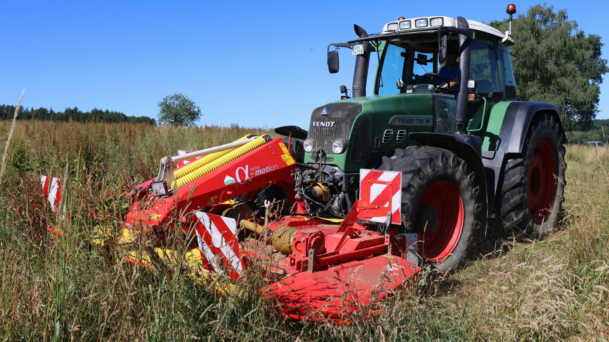 Ein Traktor mäht eine Wiese mit hohem Gras.