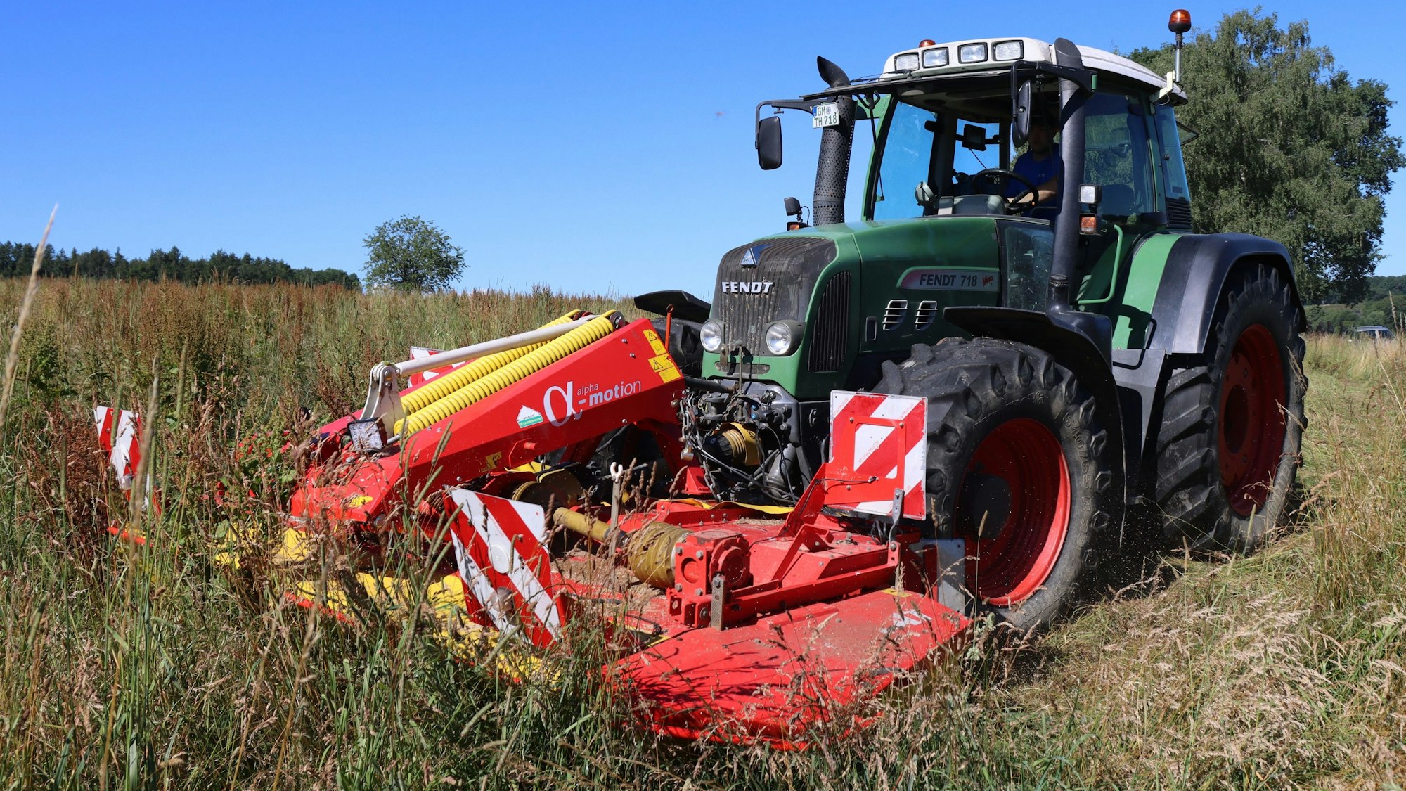Ein Traktor mäht eine Wiese mit hohem Gras.