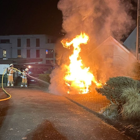 Das Foto zeigt Feuerwehrleute, die ein brennendes Auto löschen