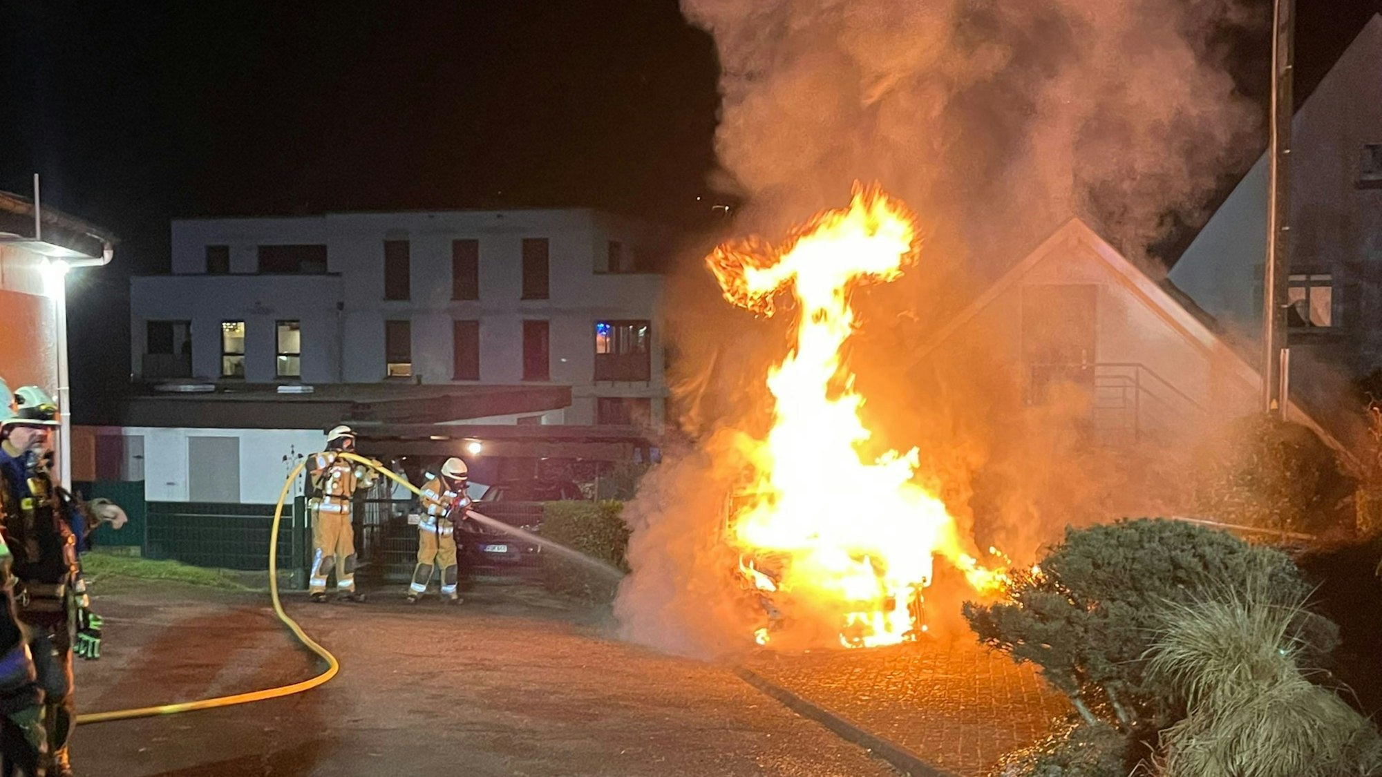 Das Foto zeigt Feuerwehrleute, die ein brennendes Auto löschen