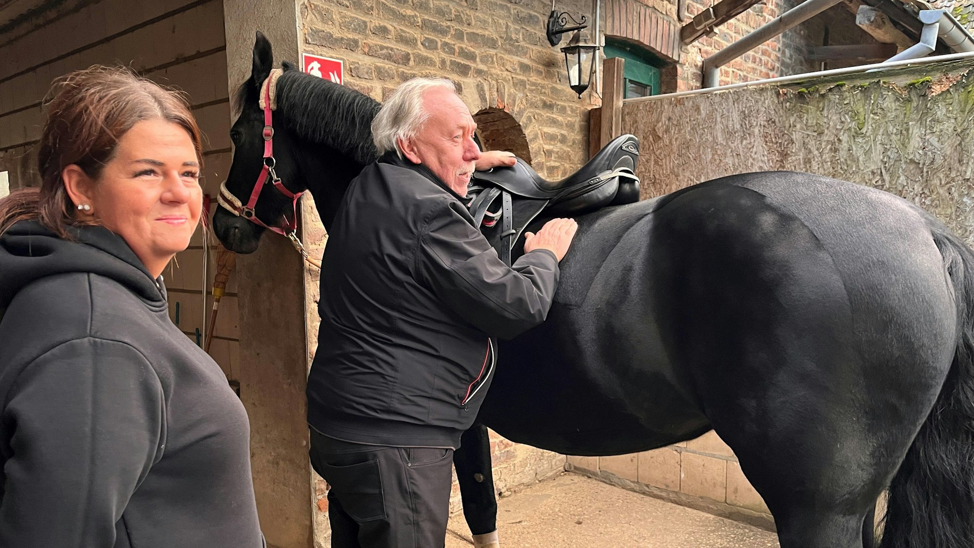 Jo Viehoff überprüft den Sattel auf dem Pferd, Reiterin Steffi Jaskowiak schaut zu.