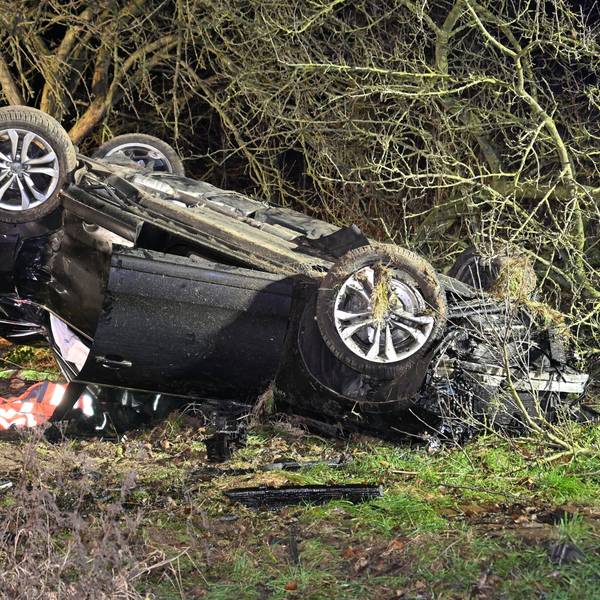 Ein schwarzes Auto liegt auf dem Dach und völlig zerbeult in einem Busch.