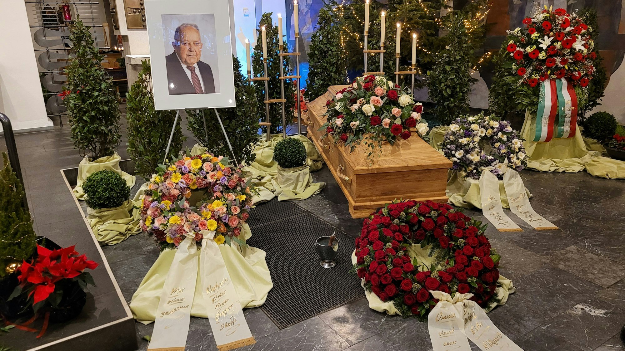 Das Bild zeigt die Trauerhalle mit dem Sarg, Kränzen und einem Porträt von Bernhard Worms.