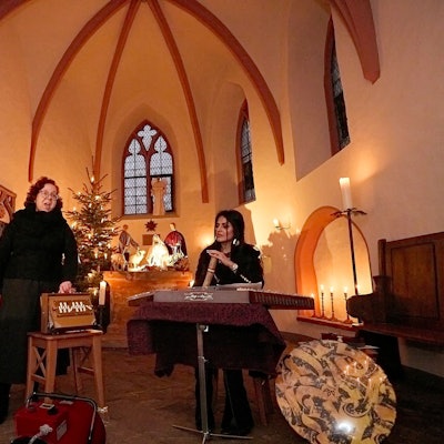 Die Musikerinnen Beate Alsdorf und Arezoo Resvani stehen in der von Kerzen erleuchteten Ahekapelle bei Engelgau im Altarraum, im Hintergrund ist ein Weihnachtsbaum.