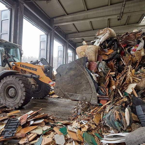 Mit einem Bagger wird im Abfallwirtschaftszentrum des Kreises Euskirchen in einer Halle Müll zusammengeschoben.