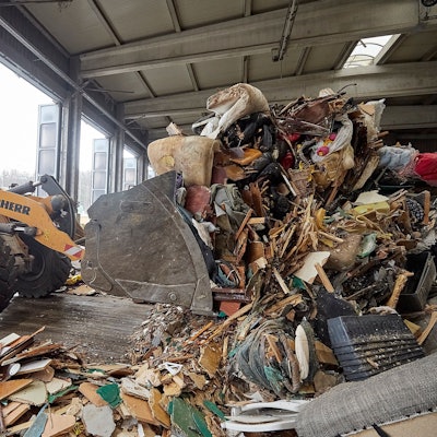 Mit einem Bagger wird im Abfallwirtschaftszentrum des Kreises Euskirchen in einer Halle Müll zusammengeschoben.