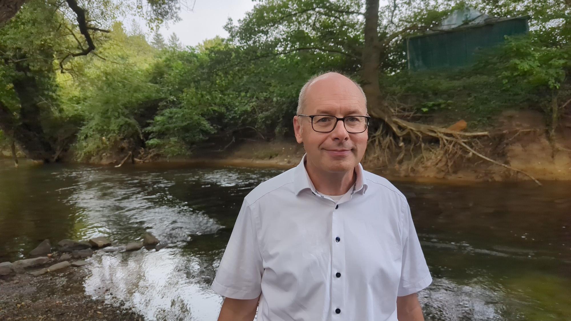 Holger Schüttrumpf steht lächelnd vor einem kleinen Fluss.