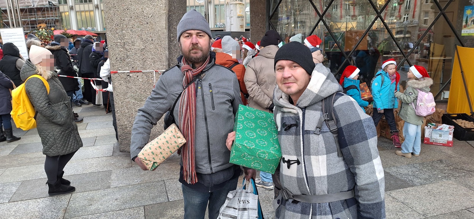 Zwei Menschen tragen Mützen und Winterjacken und halten jeweils einen Geschenkkarton im Arm.